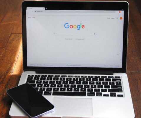 A laptop displaying the Google homepage is on a wooden surface, with a smartphone placed on the keyboard—perfect for searching home services or finding contractors’ websites. a laptop with a cell phone